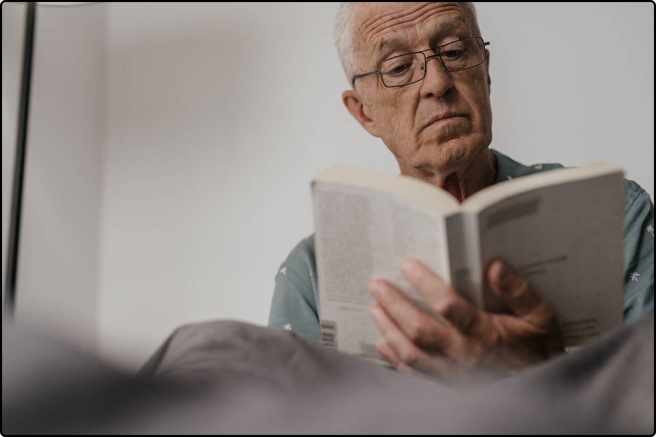 Close-up of an elderly man wearing eyeglasses, reading a book